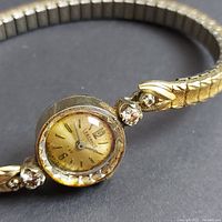 Close view of watch face showing patinated champagne dial, brand marking, applied indices, and faceted bezel.