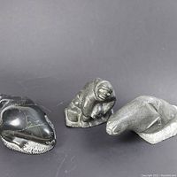 Three small Inuit carvings: seal, human figure, and bear side-by-side with green apple for scale.