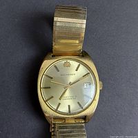 Front view of watch showing gold plated cushion case, champagne dial with Bucherer logo, applied indices, hands, and date window.