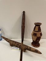 Photo showing the wooden lizard, wooden mask, and handwoven vessel together on white background for scale and identification
