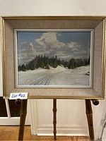 Framed painting showing snowy landscape with trees, clouds, and trail.