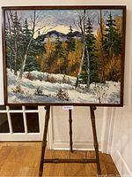 Full view of framed oil painting on an easel against wall