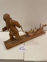 Side view of signed Indigenous wood carving showing figure pulling sled mounted on wooden base.