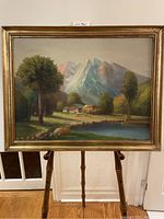 Frontal image of the framed landscape painting showing overall condition and details of the scene with pond, trees, houses, and mountains.