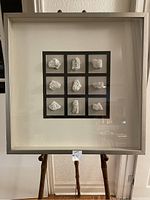 Front view of the shadow box showing nine white quartz stones arranged in a 3 by 3 grid with black matte borders, set inside a square light grey frame.