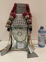 Front view of the vintage Tibetan headdress on a glass head with a water bottle for scale.