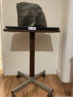Front view of the grey granite stone sculpture on a black marble base placed on a metal table with wheels, showing overall size and structure.