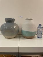 Front view of two vases and water bottle for size reference. Left vase is glazed grey and round. Right vase has textured white top, teal band middle and brown bottom with uneven rim.