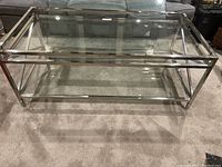 Full view of rectangular coffee table with chrome frame and two clear glass surfaces on carpeted floor.