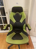 Front view of the green and black gaming chair showing ergonomic design and padded armrests.