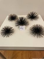Five metal starburst decorative objects placed on a white table.