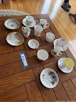 Overall assortment of tea cups, creamers, sugar dishes, and plates arranged on wooden table showing various floral patterns and styles.