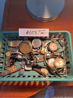 Overhead view of rectangular basket containing a mixed lot of wristwatches on wooden table