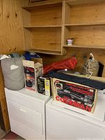 Full shot of assorted camping lot on laundry machines including sleeping bags, boxed Colemen stoves, and lantern.