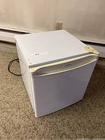 Closed white Danby mini fridge with power cord on carpeted floor.