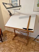 Full view of drafting table with tilted white board surface, attached adjustable arm lamp, and T-square ruler on top.