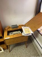 Wooden sewing table with hinged top open to reveal Kenmore sewing machine inside. Small boxes and manuals on top.