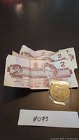 Three 1986 Canadian Two Dollar bills and one 1950 Whitehorse Klondike Dollar coin in plastic sleeve on black surface