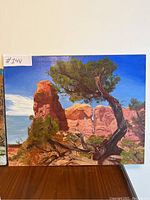 Front view of the landscape painting showing tree and rock formations under blue sky.