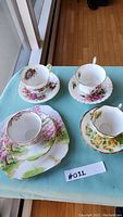 Four tea cups with matching saucers and one luncheon plate arranged on blue cloth.