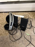 Photo shows Sennheiser braded headphones with cushioned ear pads and Edifier speakers with visible wires on a carpeted floor.