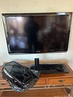 Front view of Sharp LCD TV mounted on wall with TV base and stand parts on furniture below.