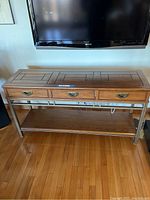 Front view of the sofa table showing three drawers with metal handles, wooden top with geometric pattern, metal frame, and lower wooden shelf.