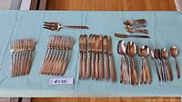 Complete set of 8 place settings with forks, knives, spoons, teaspoons, serving fork, and serving spoon laid out on light blue tablecloth