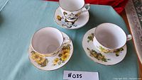 Three china tea cups and saucers with floral patterns and gold trim on a blue tablecloth.