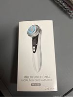 Photo of new, unopened multifunctional facial skin care massager in its original white packaging, model W-618.