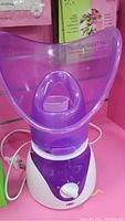 Photo of the purple and white facial steamer showing the mist shield, base with control dial, and power cord.