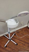 Side view of facial steamer with control panel and magnifying lamp arm extended, plugged into wall outlet.