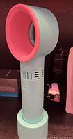 Front view of the handheld lash fan in light blue with pink fan head and power button.