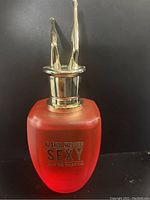 Photo of a red frosted glass perfume bottle labeled G for Women SEXY Eau de Parfum, with a gold topper shaped like two legs pointing upward.
