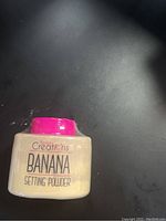 Small container of Beauty Creations Banana Setting Powder unopened with pink lid on dark surface.