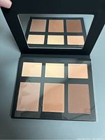 Open contour palette showing six rectangular powder pans in a range of beige to brown contour and highlight shades with a mirror inside the lid.
