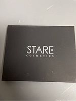 Closed black rectangular compact with STARE COSMETICS printed in white on lid.