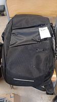 Black backpack with front zippered pocket and reflective strip on bottom showing condition and design.