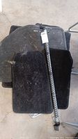 Photo showing multiple black carpet car mats stacked with visible pet hair and dirt along with a black metal anti-theft steering wheel lock bar placed on top.