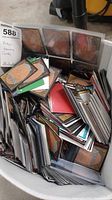 Top-down view of a large plastic container filled with loose Magic cards showing card backs and pile depth