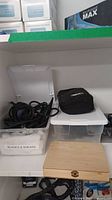 Overview of storage shelf showing plastic containers with blades and shears, cords, black pouch, and wooden box.
