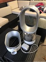 Full view of Dyson humidifier with extra bladeless loop assembly and power adapter on black woven table with beige sectional sofa in background.