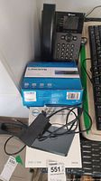 Polycom phone sitting on a box with Linksys ethernet box underneath and Dell slim USB DVD drive with cables