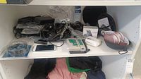 Shelf with Power Locus headphones, phone accessories, various cords and cables, and a white Samsung smartphone.