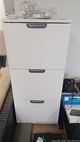 Front view of white 3-drawer file cabinet with combination lock, showing three drawers with recessed handles.