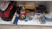 Wide shot showing the tool bag, rolls of tape, glue, sanding block, sponges and various small hardware items spread on shelf.