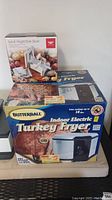 Box of Butterball Indoor Electric Turkey Fryer and original box of Spiral Vegetable Slicer sitting side by side on a dark surface.