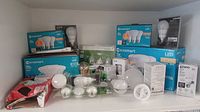 Wide shot showing multiple boxes and loose light bulbs on a shelf. Includes Ecosmart LED multi-packs as well as bulb sleeves and blister packs.