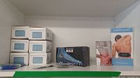 Photo showing Medicpad Ultramax and Medicpad back pain relief devices in packaging alongside Medicpad foot device and multiple boxes of face masks on a shelf.