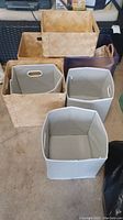 Nine various storage bins including collapsible fabric bins and woven wood baskets arranged on floor.